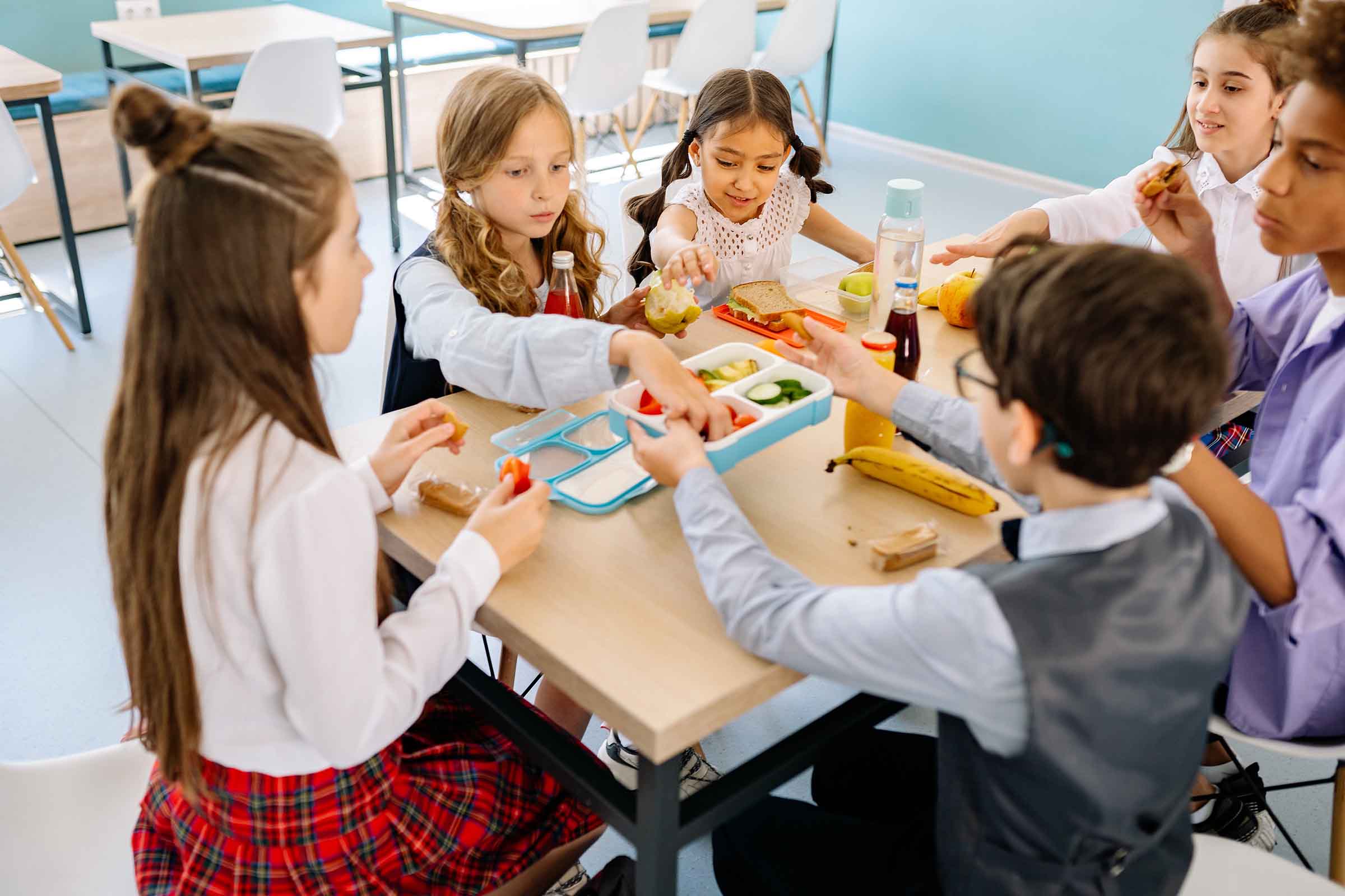children sat around school table eating lunch